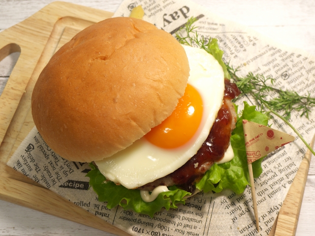 上から見たハンバーガー。バンズがズレて目玉焼きが見えている。その下にはタレのかかったパテが見える。